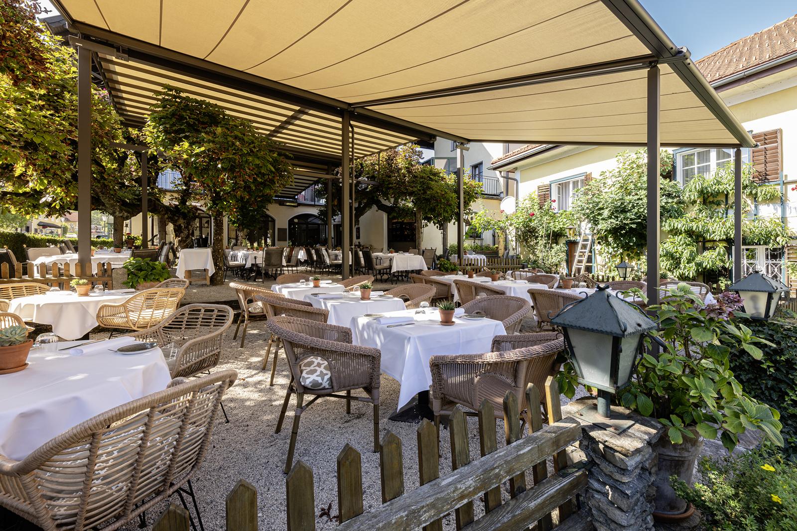 Een hotelterras met gedekte tafels onder grote pergola-zonneschermen van markilux