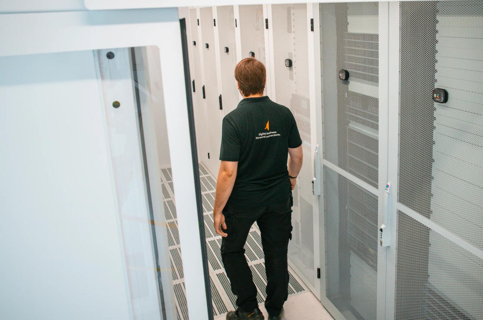 Een technicus van NorthC loopt door een gangpad tussen witte serverkasten